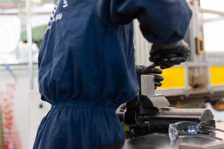 Ragazzo in tuta da lavoro blu mentre lima un pezzo di metallo in laboratorio di macchine utensili