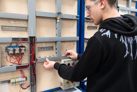 Ragazzo con occhiali protettivi che chiude le canaline dell'impianto elettrico dopo aver concluso il suo impianto industriale prima della verifica