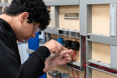 Ragazzo con occhiali protettivi che serra una vite di chiusura del cavo elettrico dell'impianto elettrico che sta realizzando