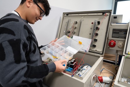 Ragazzo davanti al quadro elettrico che sta realizzando con la scatola degli indicatori da attaccare ai fili per riconoscere inizio e fine