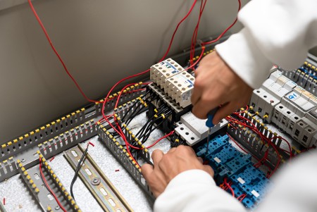 Dettaglio delle mani di un ragazzo che con il cacciavite fissa il cavo dell'impianto all'interno del quadro elettrico