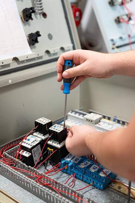 Dettaglio delle mani di un ragazzo che con il cacciavite fissa il cavo dell'impianto all'interno del quadro elettrico