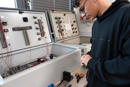 Ragazzo con occhiali protettivi prepara un filo elettrico per essere inserito nell'impianto industriale che sta preparando nel laboratorio