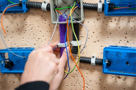 Un tecnico sta installando i cablaggi elettrici all'interno di un impianto civile, fissando i tubi corrugati e organizzando i fili all'interno di una scatola di derivazione.