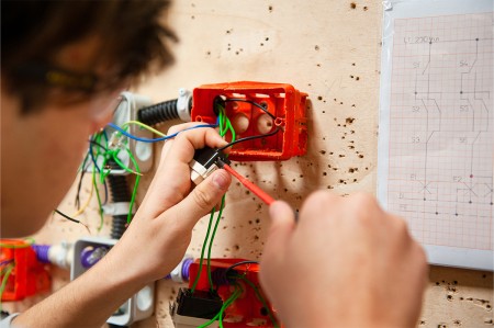 Un tecnico sta collegando i cavi elettrici a un interruttore all'interno di una scatola di derivazione, seguendo uno schema elettrico di riferimento.