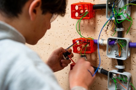 Un tecnico sta collegando i cavi elettrici a un interruttore all'interno di una scatola di derivazione, seguendo uno schema elettrico di riferimento.