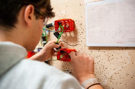 Un tecnico sta collegando i cavi elettrici a un interruttore all'interno di una scatola di derivazione, seguendo uno schema elettrico di riferimento.