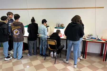 Gruppo di studenti impegnati in attività creative, disposti attorno a un tavolo con box fotografici illuminati. Alcuni ragazzi stanno osservando e lavorando su piccoli progetti esposti sotto le luci.