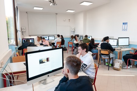 Studenti in un'aula informatica lavorano ai loro progetti utilizzando computer desktop, in un ambiente di apprendimento collaborativo.